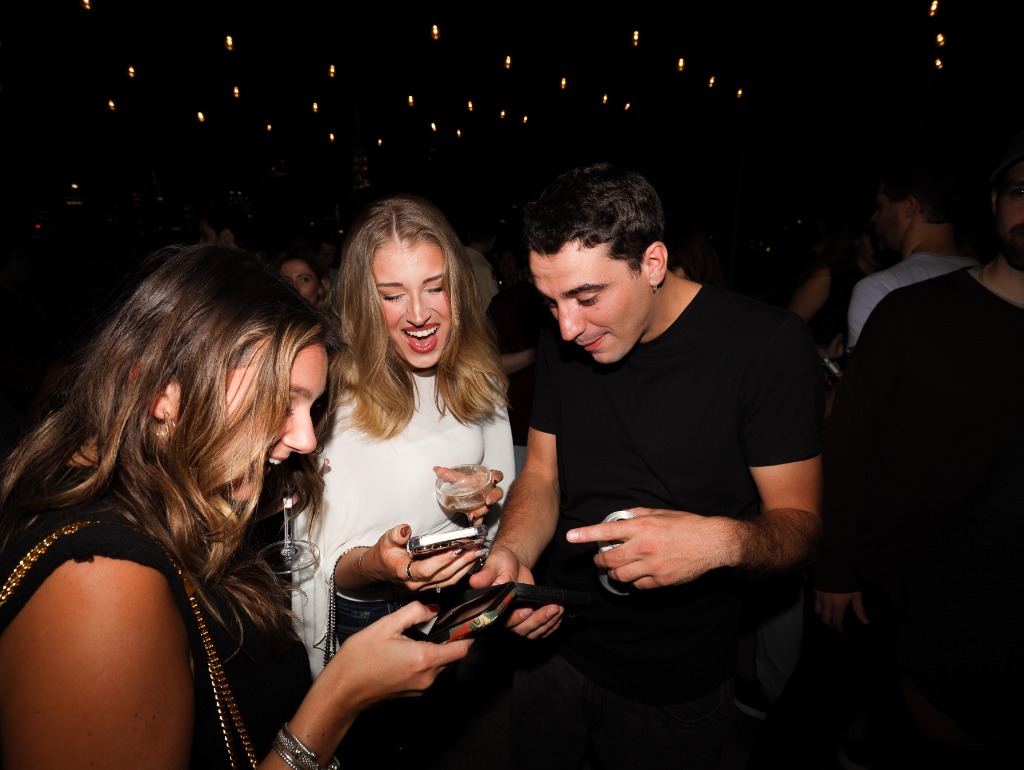 Friends laughing and looking at phone at outdoor evening event